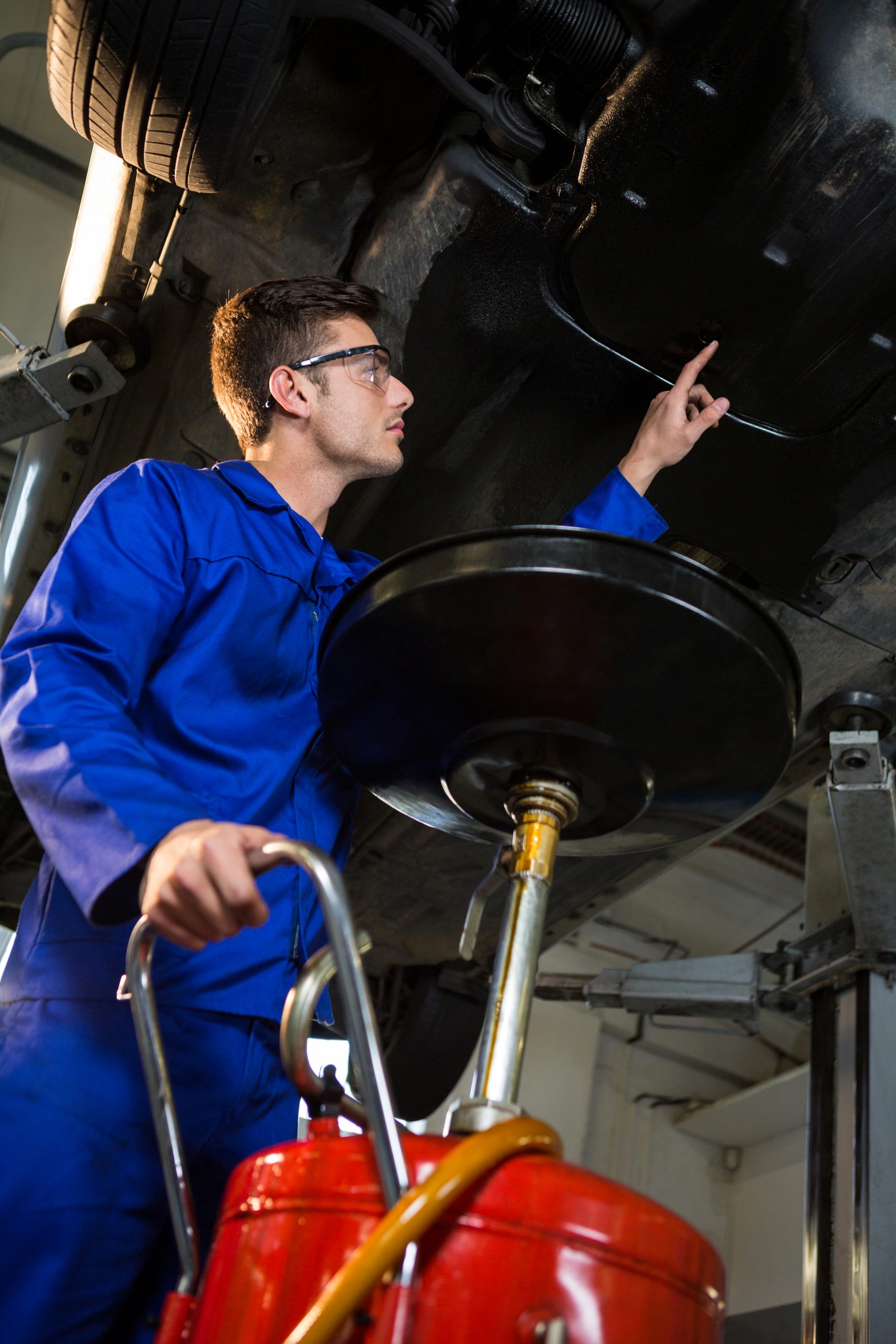 Certified auto mechanic performing an oil change and lube service under a lifted vehicle in a professional repair garage