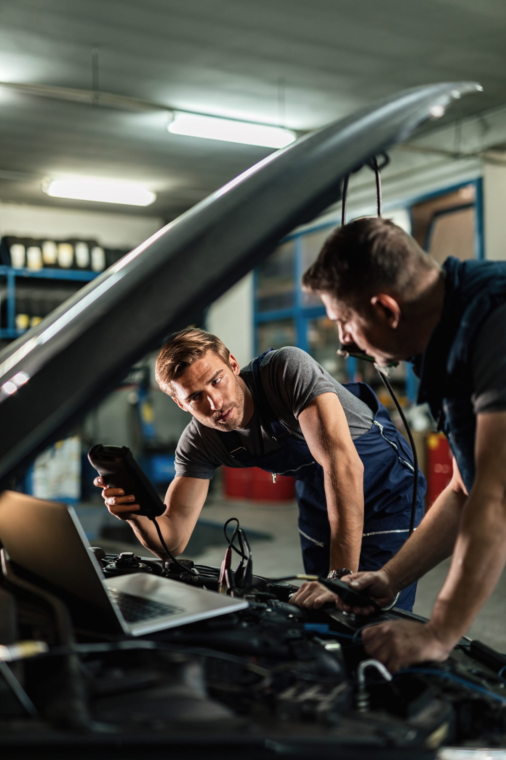 Mechanics inspecting a car engine and discussing diagnostic results in an auto repair shop